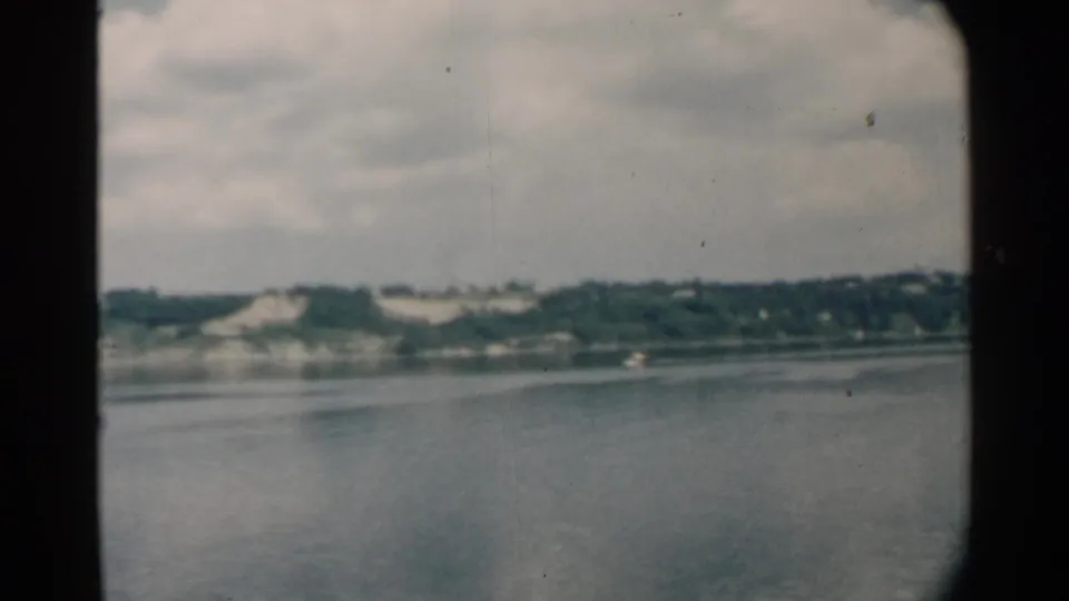 Pearl Harbor shoreline appears beyond calm water in this 1958 8mm passenger-window view.