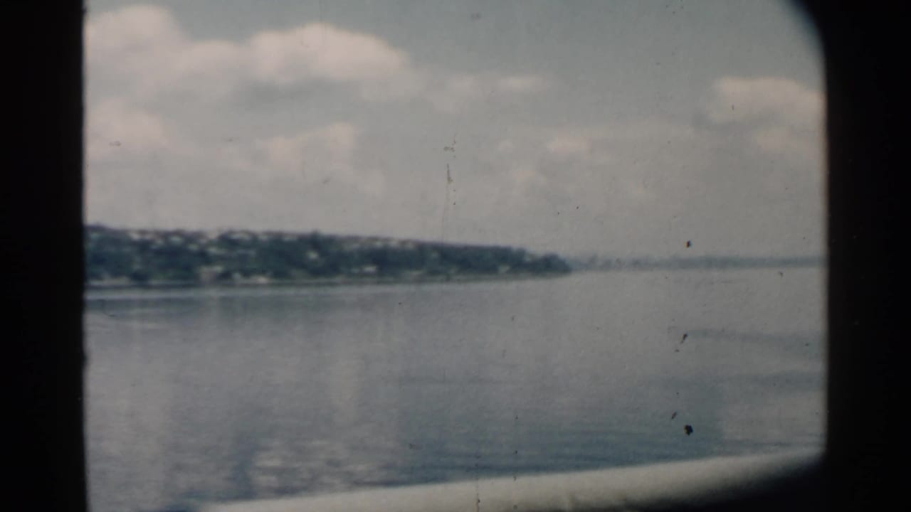 Home-movie frame looking across smooth Hawaii harbor water, with distant shore fading toward the right horizon.