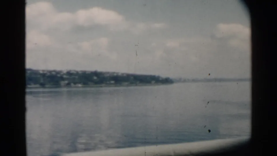 Home-movie frame looking across smooth Hawaii harbor water, with distant shore fading toward the right horizon.
