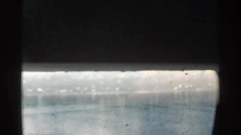 Partly obscured 8mm frame with sun glare on the water and dark film or window edge across the upper view.