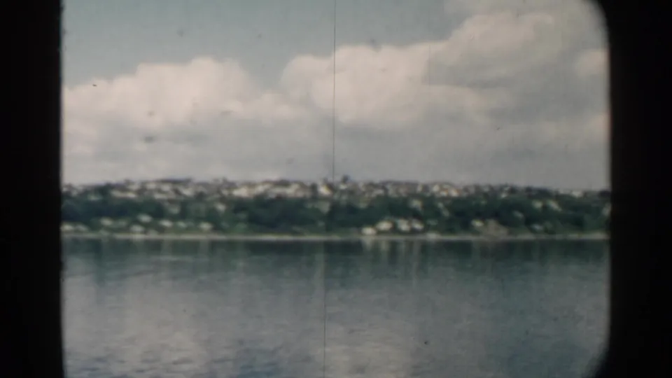 1958 home-movie view of a Pearl Harbor-area shoreline with scattered distant houses across calm water.