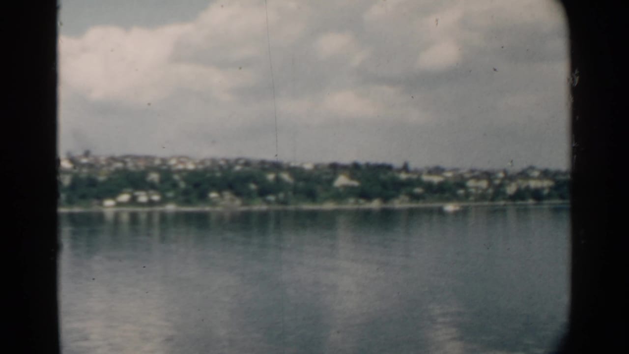 Wide harbor view with distant houses, trees, and cloud reflections on the water.