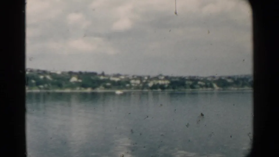 Soft 8mm frame of Pearl Harbor water and a distant 1958 shoreline with small buildings and trees.