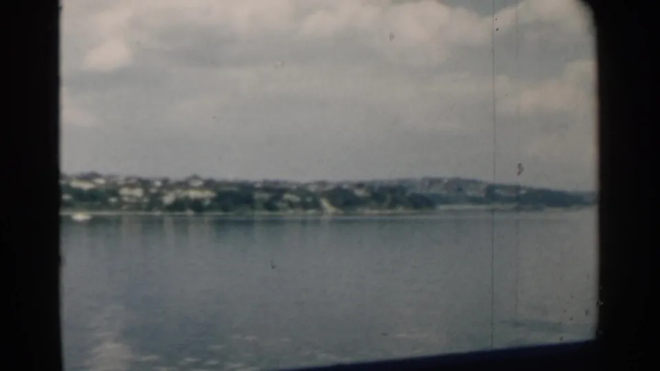 Final 1958 Pearl Harbor frame showing calm water, a distant shoreline, low hills, and cloudy sky from a vessel viewpoint.