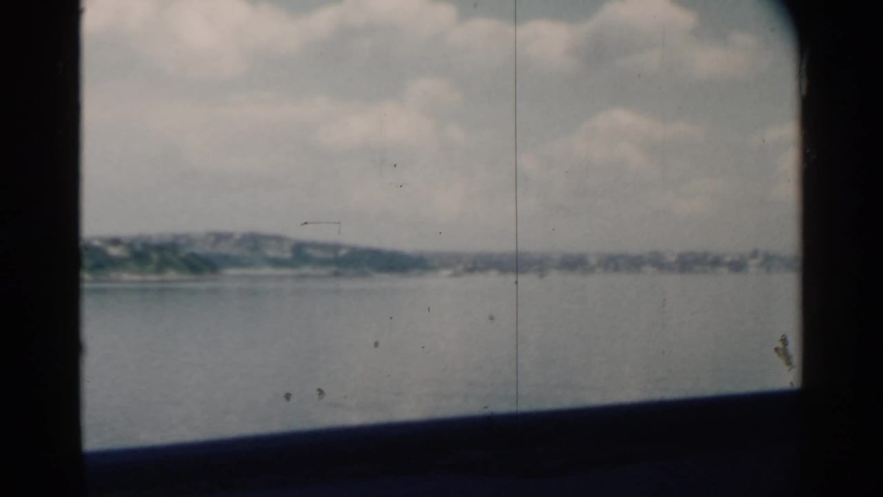Distant shoreline and open water seen through dark boat window framing.
