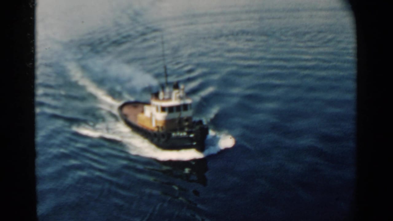 Small tugboat crossing dark blue water with a white wake behind it.