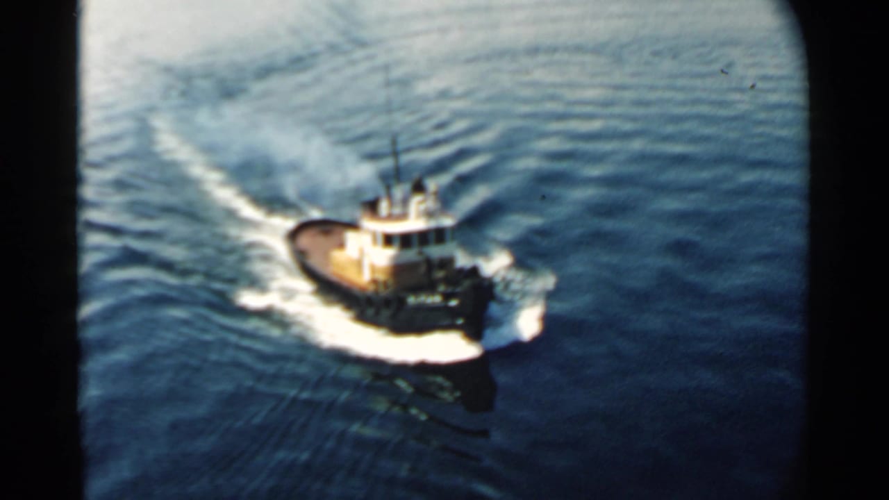 Small tugboat in Pearl Harbor, Hawaii, seen from above as it moves through rippled blue water in 1958 footage.