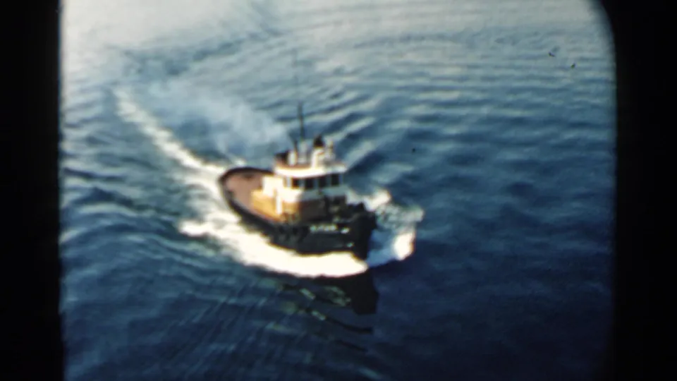 Small tugboat in Pearl Harbor, Hawaii, seen from above as it moves through rippled blue water in 1958 footage.