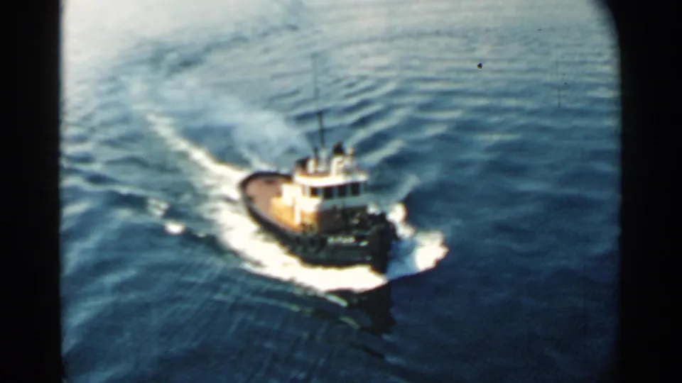 Closer 8mm view of a tugboat moving across Pearl Harbor water, with white wake and soft film grain visible.
