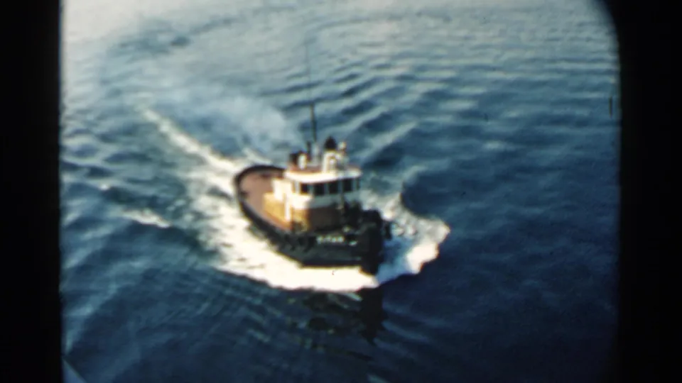 Pearl Harbor tugboat frame from 1958 showing the vessel moving through calm water with curved white wake patterns.