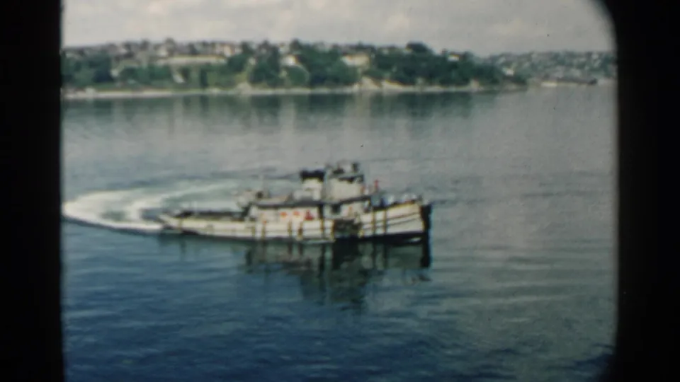 A small steam-powered ferry or tug appears closer in frame as it crosses the Pearl Harbor-area water in 1958 home-movie footage.