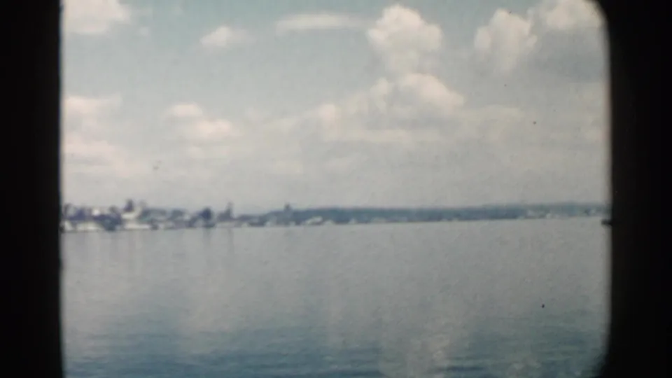 A wider 1958 Pearl Harbor-area harbor view shows open water, a distant low cityscape, and a partly cloudy sky.