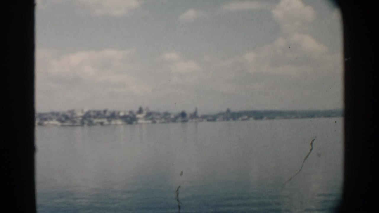 Soft waterfront panorama with distant buildings across smooth blue water.