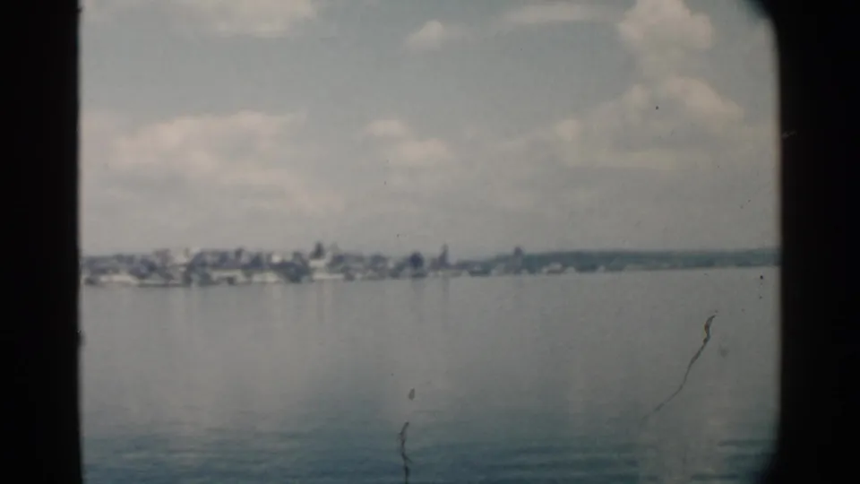 Pearl Harbor, Hawaii frame with a distant shoreline across still water, partly cloudy sky, and visible 8mm film scratches and gate edges.