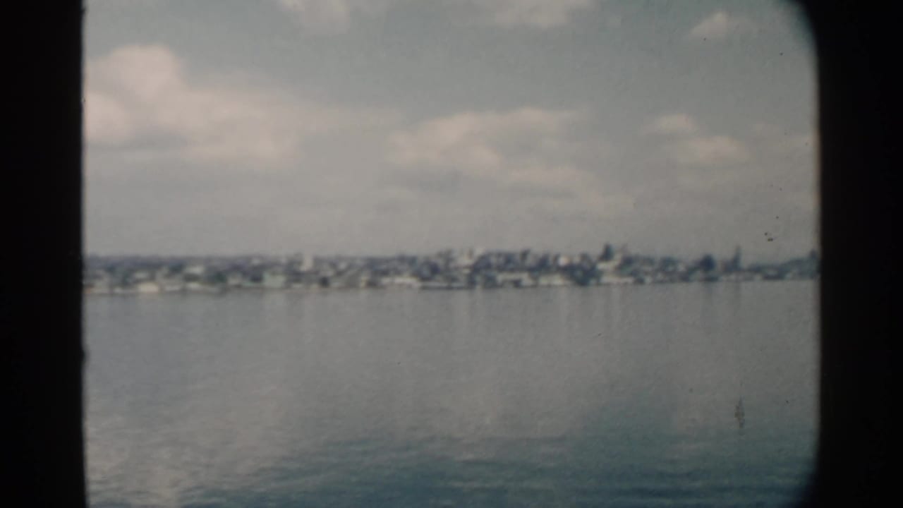 Distant shoreline homes across calm harbor water under a partly cloudy sky.