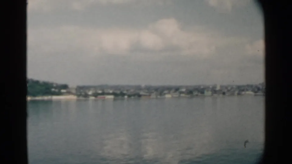 Pearl Harbor, Hawaii shoreline seen from across the water in 1958 home-movie footage, with dark frame edges and soft 8mm color.