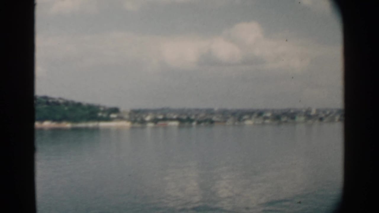 Calm harbor water with a distant green shoreline under a cloudy sky.