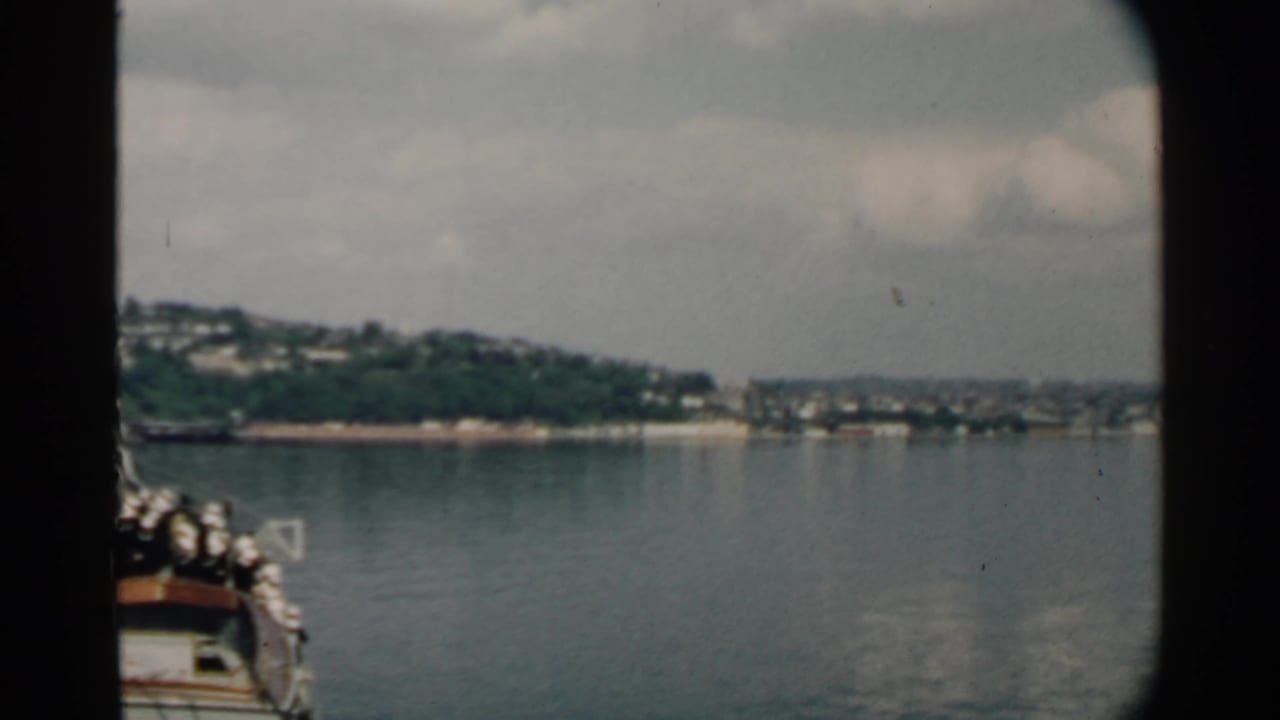 Boat bow and railings enter the frame as shoreline sits across the water.