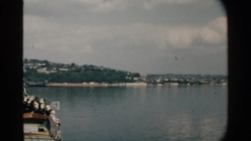 A passenger view from a moving boat toward a green shoreline in likely Pearl Harbor, Hawaii, on 8mm film.