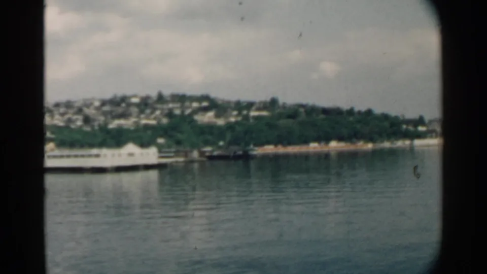 Likely Pearl Harbor shoreline with hillside homes and waterfront structures seen from a moving boat in 1958 footage.