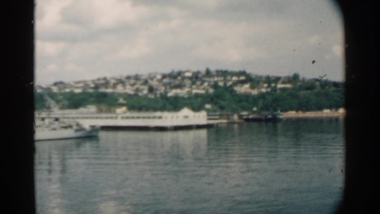 1958 Pearl Harbor footage shows a white vessel on the water with a long pier, wooded shoreline, and hillside homes in the distance.