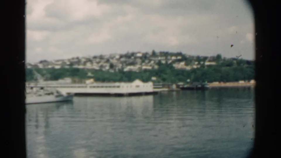 1958 Pearl Harbor footage shows a white vessel on the water with a long pier, wooded shoreline, and hillside homes in the distance.