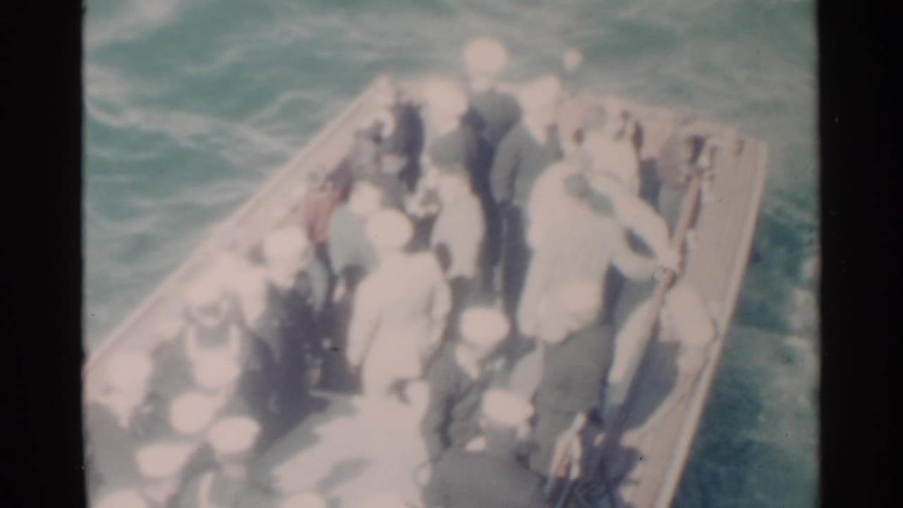 Crowded small boat with Navy personnel in white caps moving through choppy water.