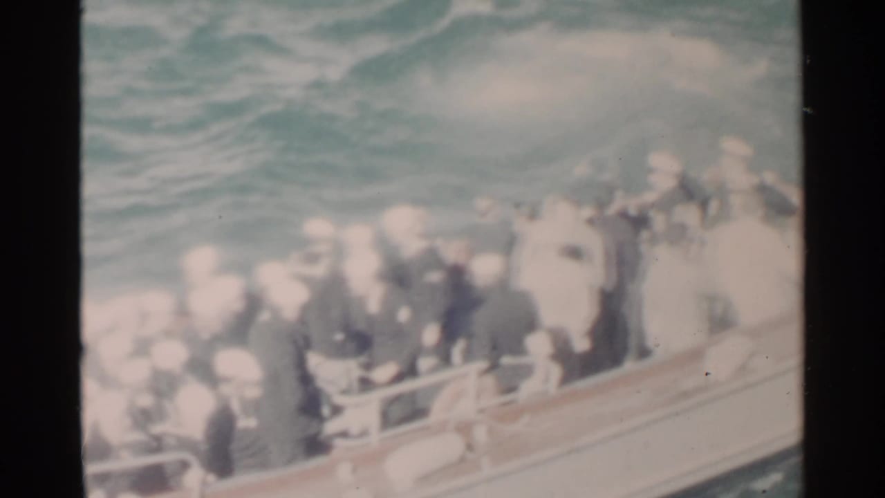 High-angle 8mm view of Navy personnel aboard a small boat near Pearl Harbor, with faces softened by exposure and motion.