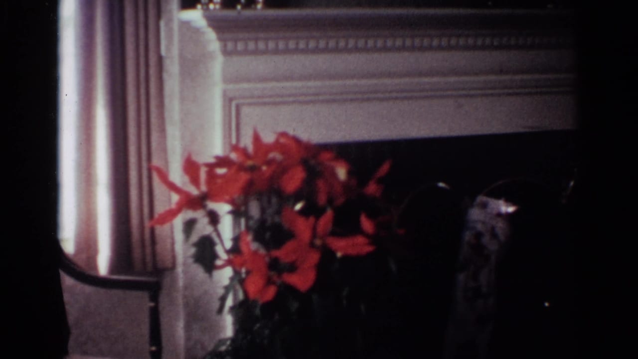 1959 Ohio home-movie frame showing a red poinsettia near a white mantel and dark fireplace in a private living room.