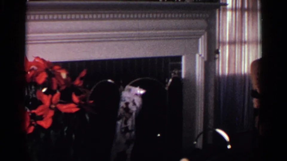 1959 Ohio home interior with a red poinsettia, white fireplace mantel, dark fireplace opening, and striped drapes at the side.