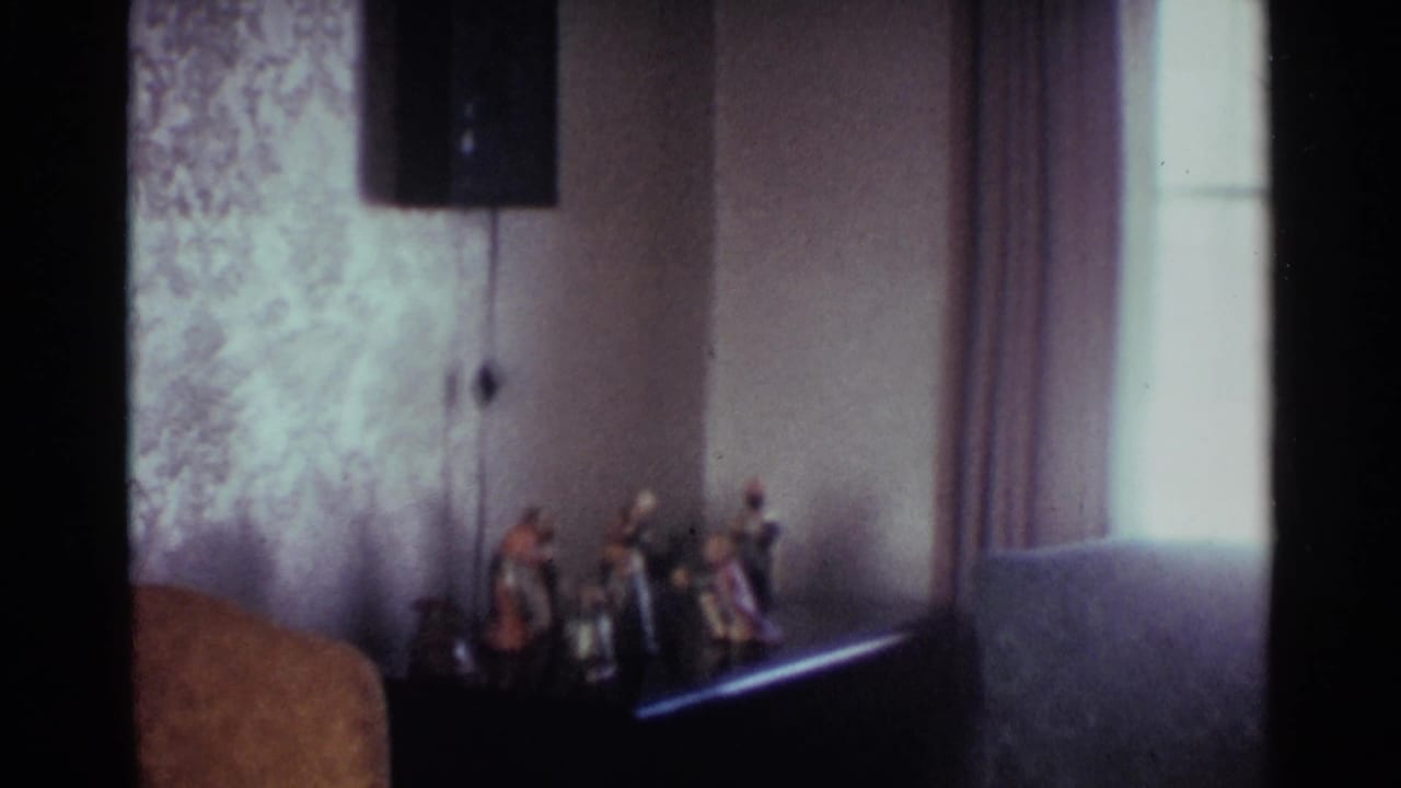 Small nativity figurines on a dark surface beside a bright window and patterned wall.