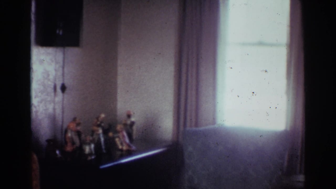 1959 Ohio interior view of a small nativity scene beside a bright curtained window in soft 8mm color.