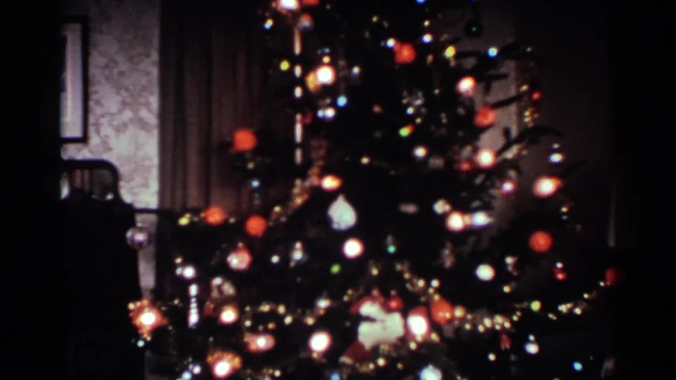 1959 Ohio home-movie frame of a decorated Christmas tree with glowing lights, ornaments, tinsel, and nearby room furnishings.