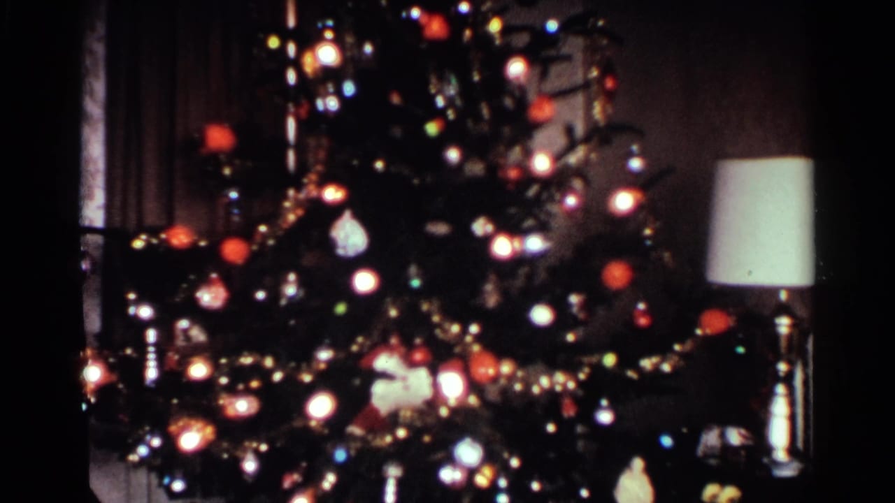 1959 Ohio home-movie frame showing a lit Christmas tree with ornaments and tinsel near a table lamp in a private living room.