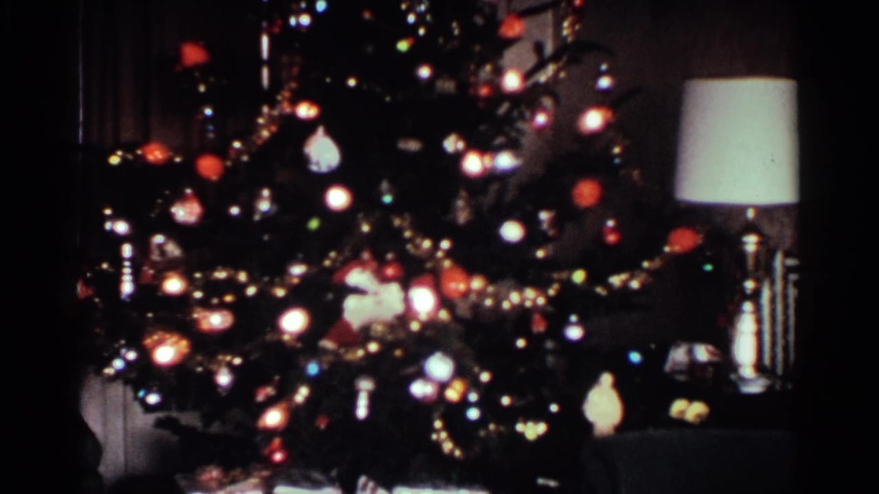 1959 Ohio home-movie frame with a decorated Christmas tree, bright lights, tinsel, and a table lamp in a private interior.