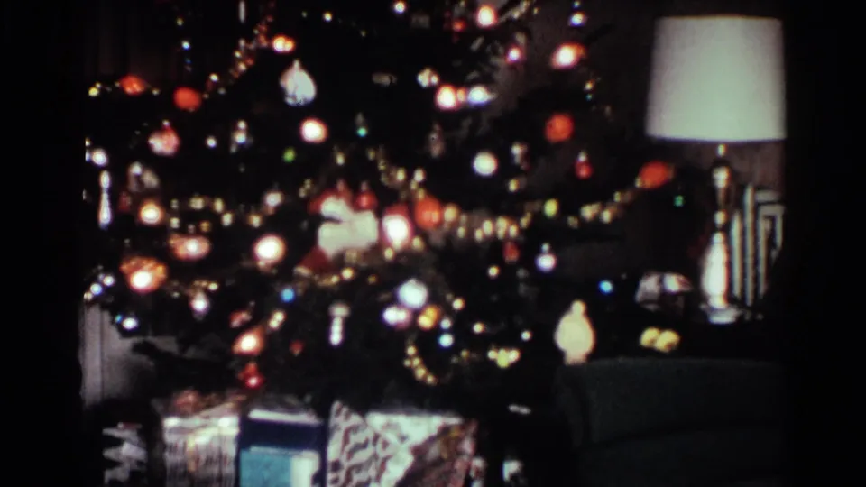 1959 Ohio home-movie frame panning down to wrapped presents beneath a lit Christmas tree in a private living room.