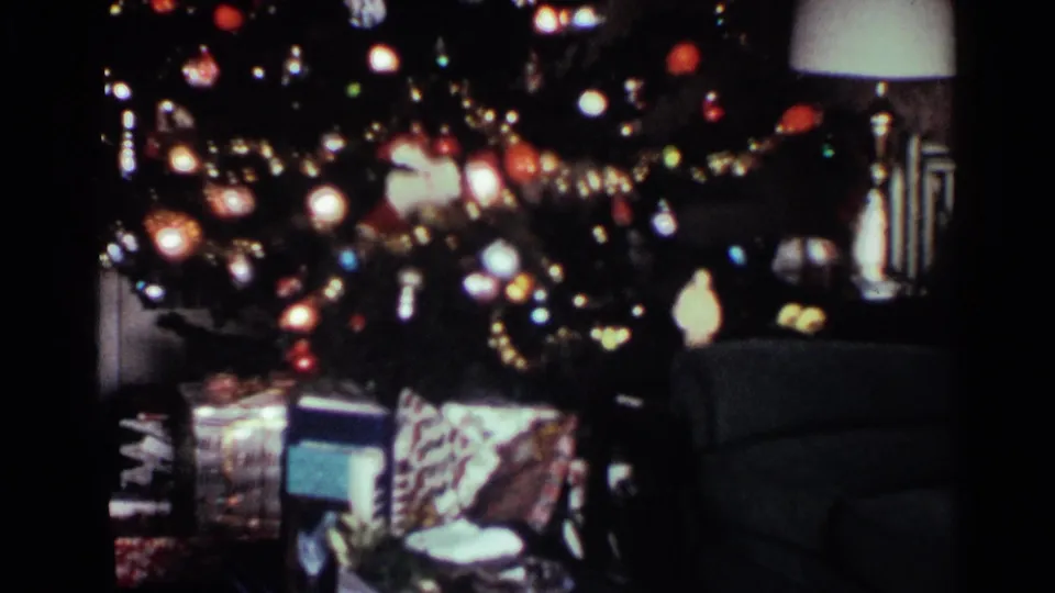 1959 Ohio home-movie frame showing presents under a decorated Christmas tree, with a lamp and upholstered furniture nearby.