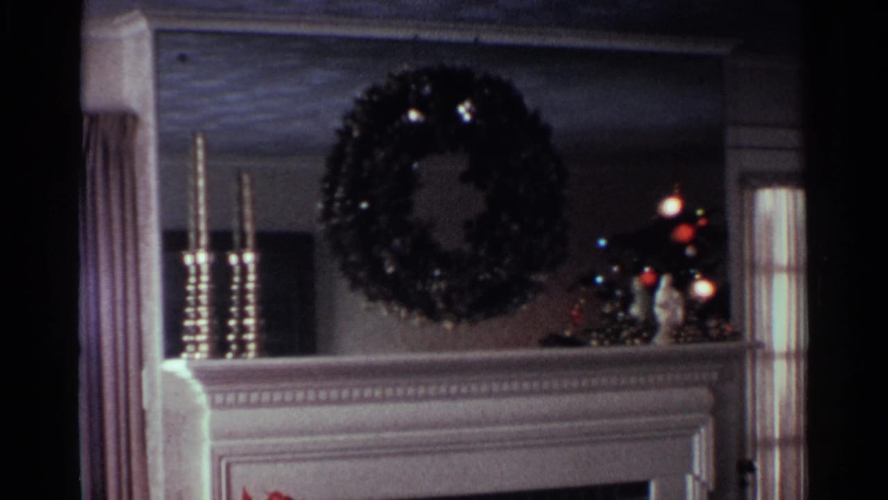 1959 Ohio home-movie frame showing an interior mantel with a holiday wreath and a window beside it.