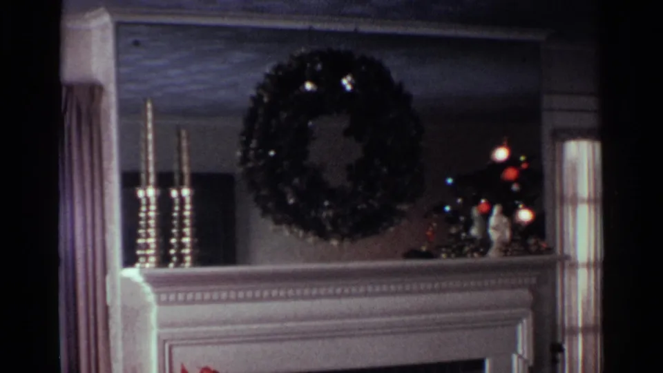 1959 Ohio home-movie frame showing an interior mantel with a holiday wreath and a window beside it.