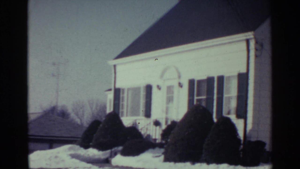 White house with dark shutters and snow-covered shrubs in the front yard.