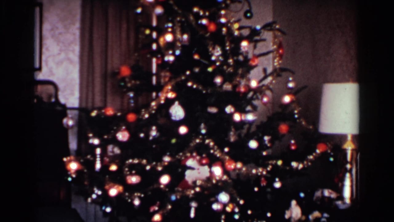 Decorated Christmas tree beside a lamp in a dim interior.