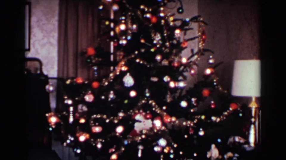 1959 Ohio 8mm frame with a lit Christmas tree, ornaments, shiny garlands, a pale lampshade, curtains, and patterned wall covering.