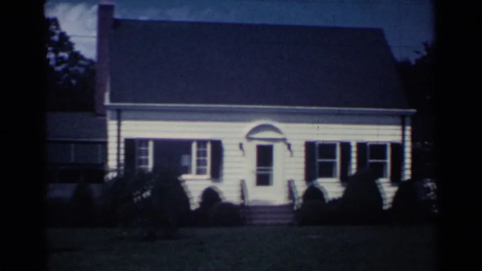 The 1959 Ohio footage shows a front-facing view of a white house with dark shutters, a small entry, steps, shrubs, and a broad lawn.