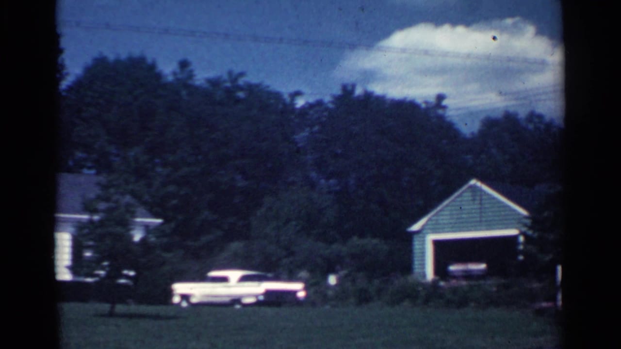 1959 Ohio residential exterior with a detached garage, trees, lawn, and a pale period vehicle near the house.