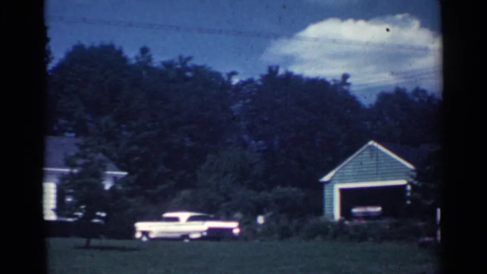 1959 Ohio residential exterior with a detached garage, trees, lawn, and a pale period vehicle near the house.