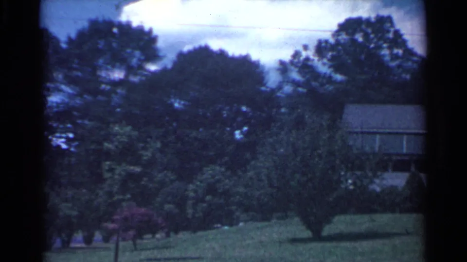 1959 Ohio 8mm frame showing a residential yard with mature trees, lawn, shrubs, and part of a house at dusk.