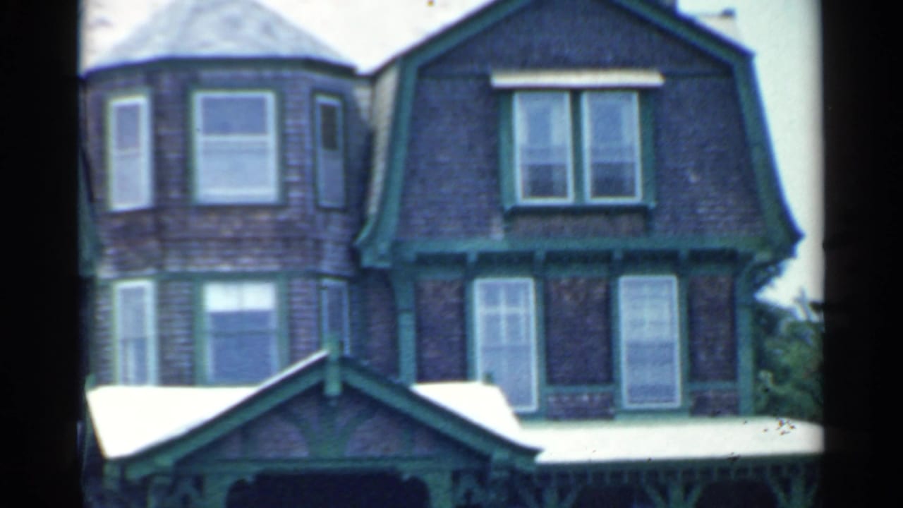 1959 San Francisco home-movie frame showing a dark wood building with green trim, tall windows, and soft motion from a passing vehicle.