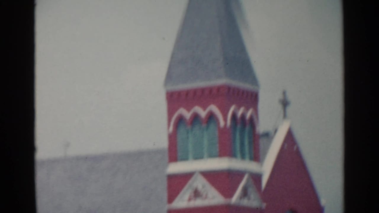 Red brick church tower with arched windows and pale trim, seen in soft focus.