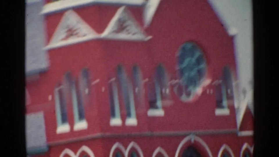 1959 San Francisco 8mm frame showing the red brick church facade, pointed trim, narrow arched windows, and a round window.