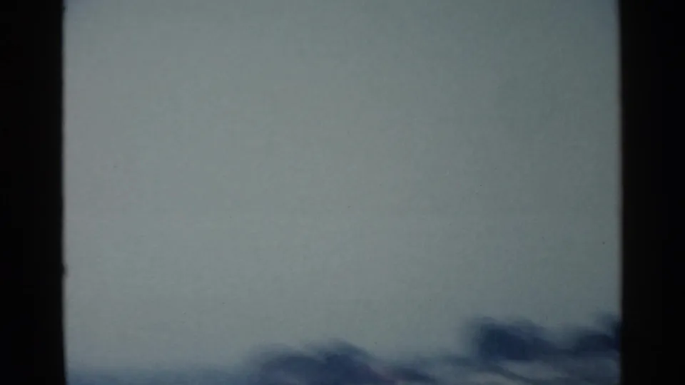 Blurred moving-vehicle frame from the San Francisco-area clip, with a dark vertical strip, pale open space, and indistinct low forms near the horizon.